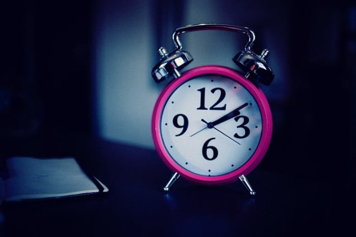 Pick clock pointing at 2:10 sitting on a table next to a file.