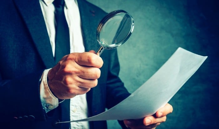 Man holding a cv for grad school holding a magnifying glass over it.
