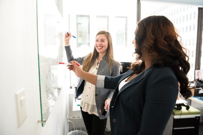 Two female MBA students solving problem on white board while smiling