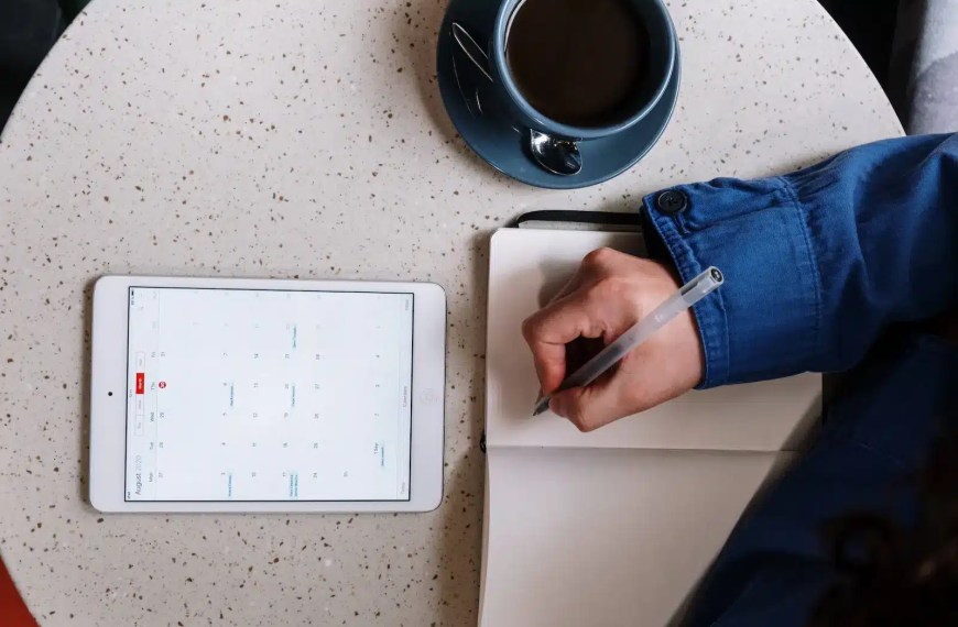 Prospetice MBA student working on his application timeline with a cup of coffee, a notebook, and an ipad