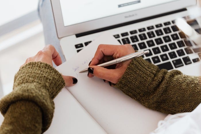 Student taking notes while looking at computer screen