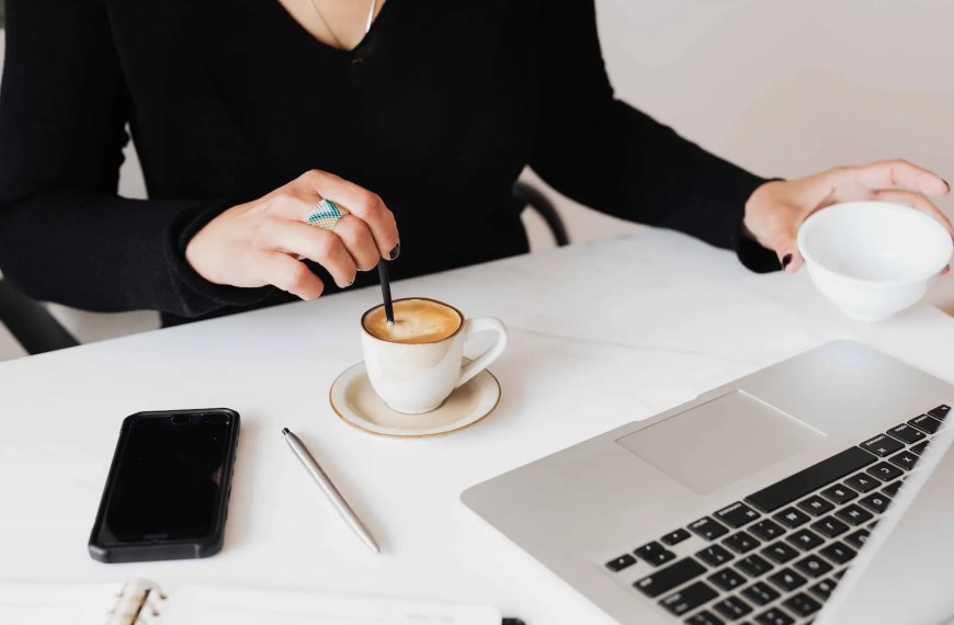 female executive having coffee at her desk looking at laptop