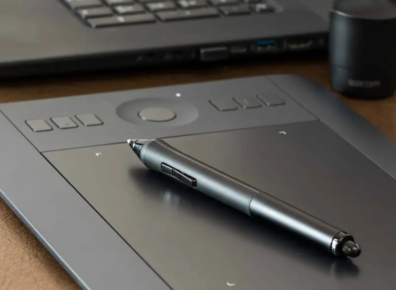 A digital pen resting on a tablet with a laptop in the background, representing tools for writing standout MBA personal statement examples.