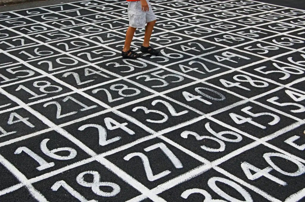 A child walking on a large painted number grid on the pavement, used for educational or recreational purposes.