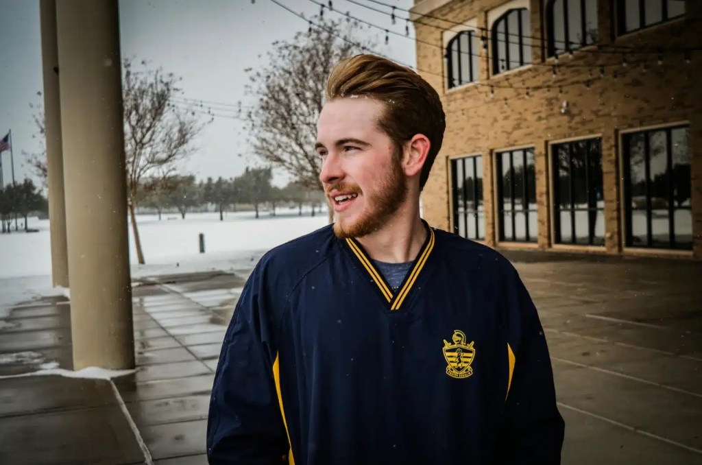 Man wearing a navy and yellow jacket standing outside on a snowy day, smiling and looking to the side.