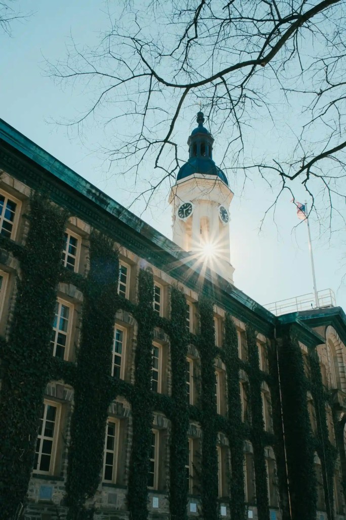 Ivy-covered university building with a clock tower, sunburst shining through, symbolizing academic tradition and new beginnings