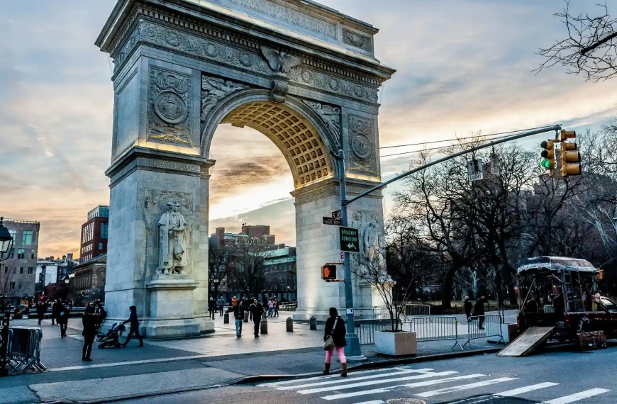 Washington Square Arch in New York City at sunset, with people walking and city buildings in the background”