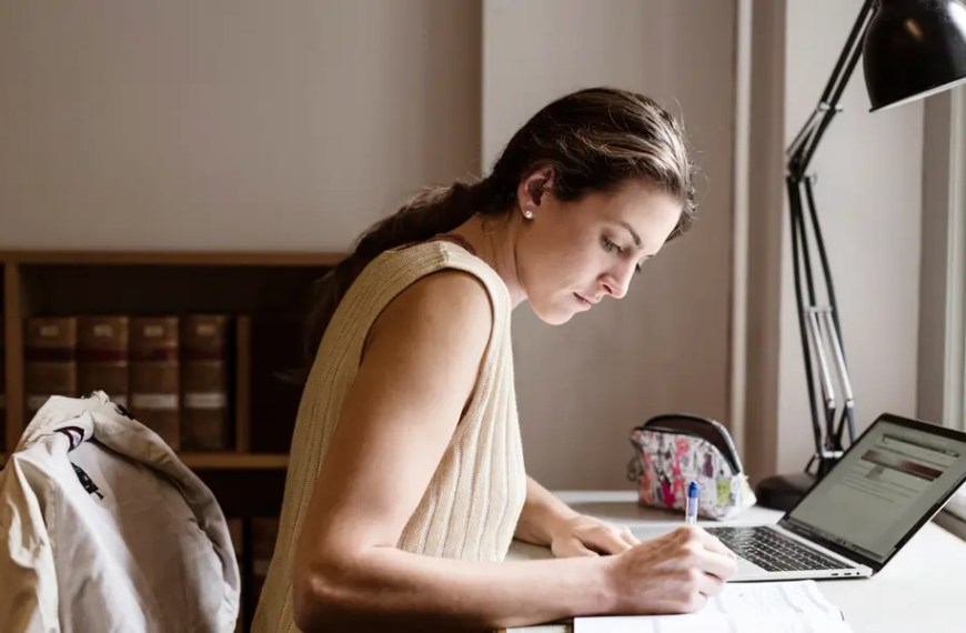 Economics PhD student studying with laptop and notes at desk