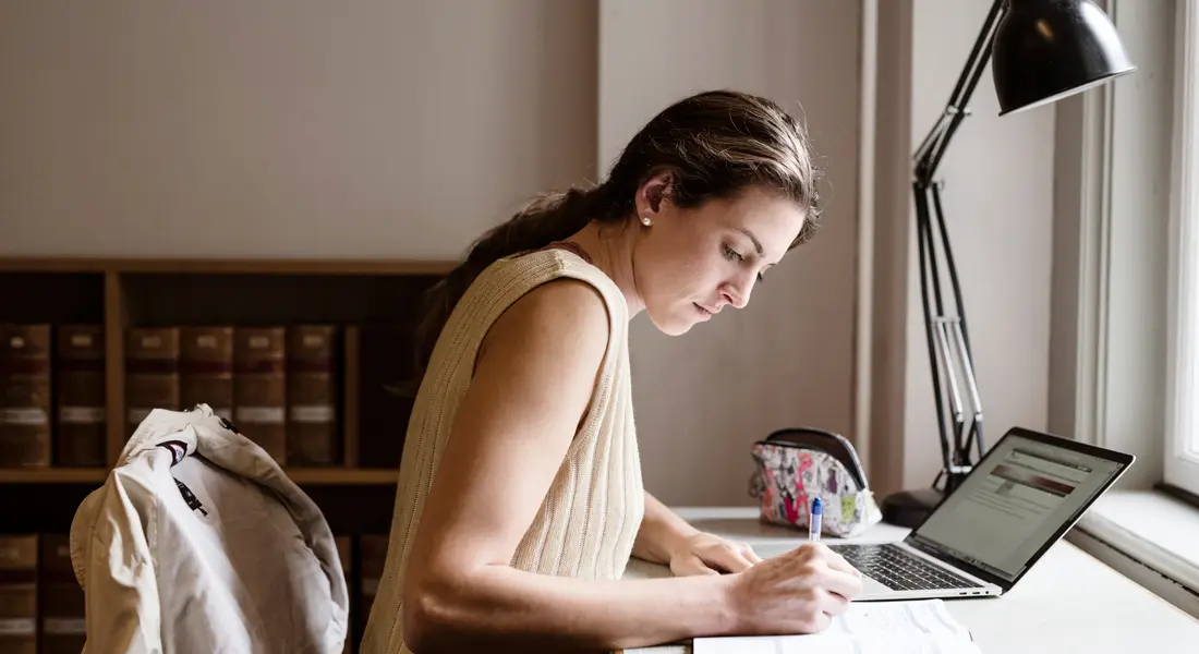 Economics PhD student studying with laptop and notes at desk
