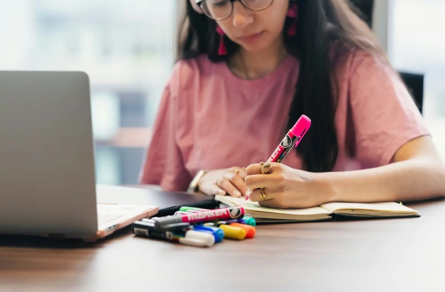 Student writing a UK PhD research proposal at a desk with laptop and notebook, preparing research statement and research interests